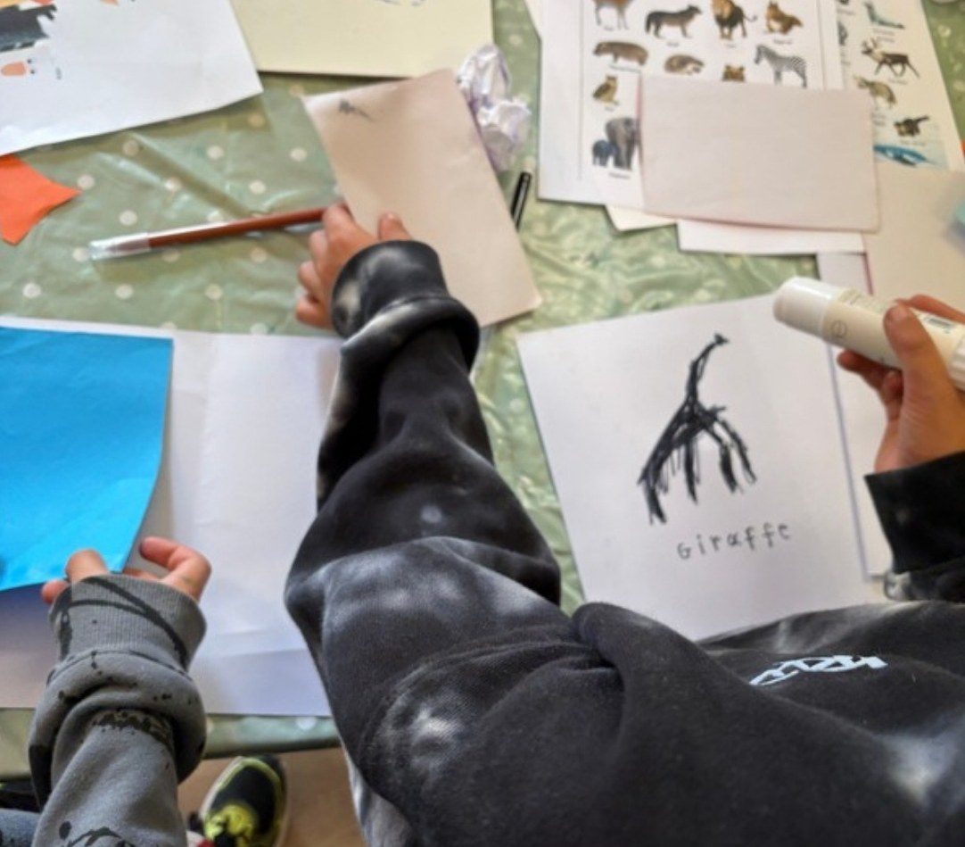 Children drawing animals, with a giraffe picture on the table